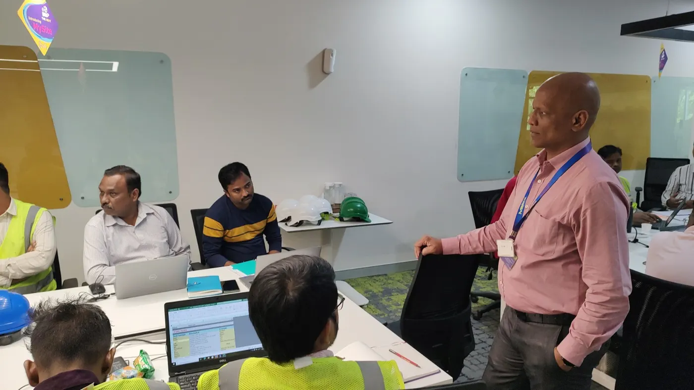 Trainer briefing a manufacturing team wearing safety helmets around a conference table